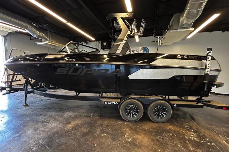 The Image of 2025 Supra SE boat in showroom, sleek black design on trailer. - 1