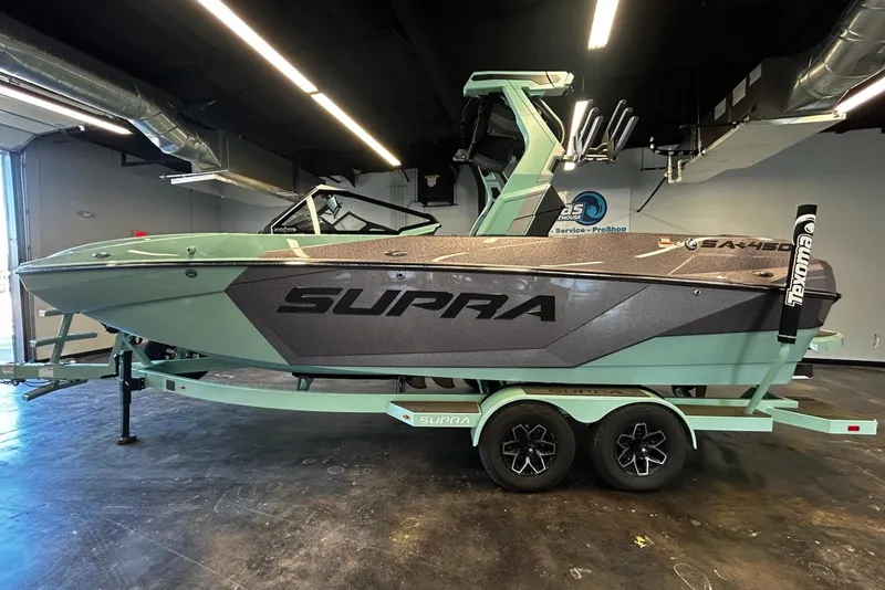 The Image of 2025 Supra SA boat in showroom, mint green and black design, on a trailer. - 1