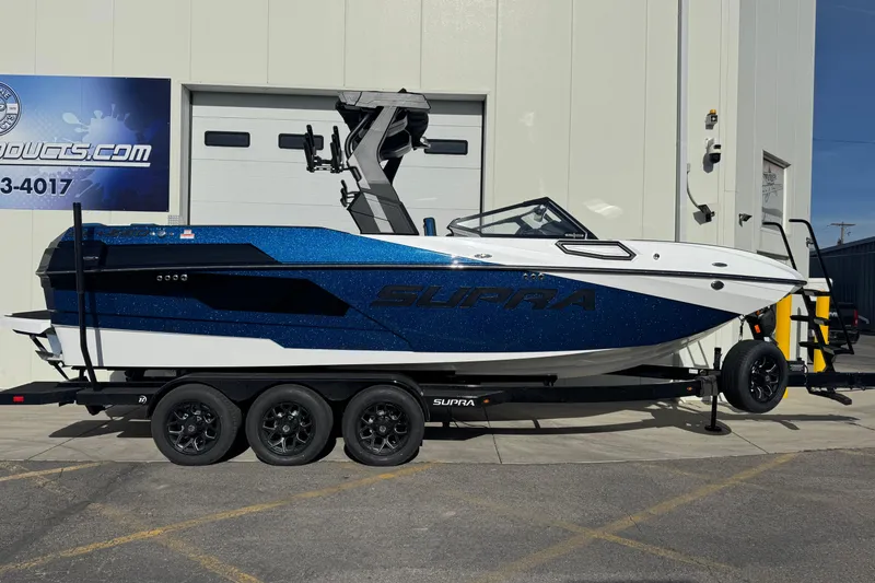 Slide: The Image of 2026 Supra SE 575 boat on trailer, blue and white design, parked outside a building. - 9