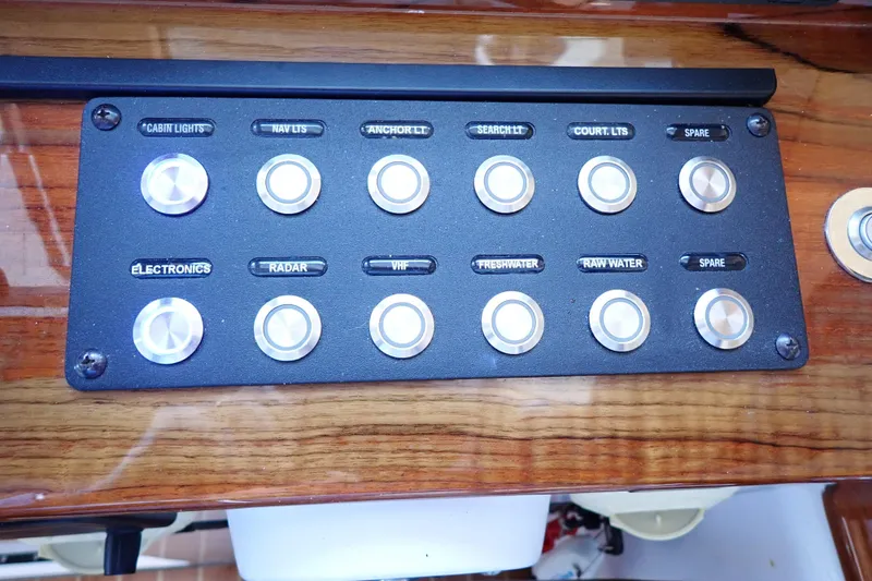 Slide: The Image of Control panel of 2023 True North 34 Outboard Express with labeled switches on wood finish. - 49