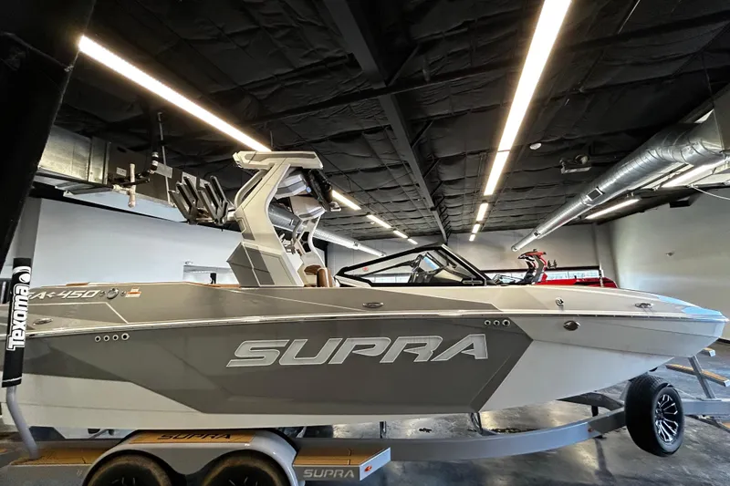 Slide: The Image of 2025 Supra SA boat in showroom, sleek design, gray exterior, on trailer. - 2