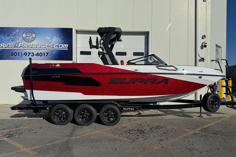 Slide: The Image of 2026 Supra SE 575 boat in red and white on a trailer outside a building. - 3