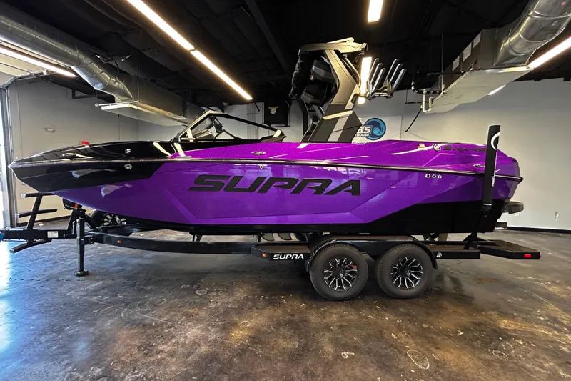 The Image of 2025 Supra SA boat in vibrant purple, displayed indoors on a trailer. - 1