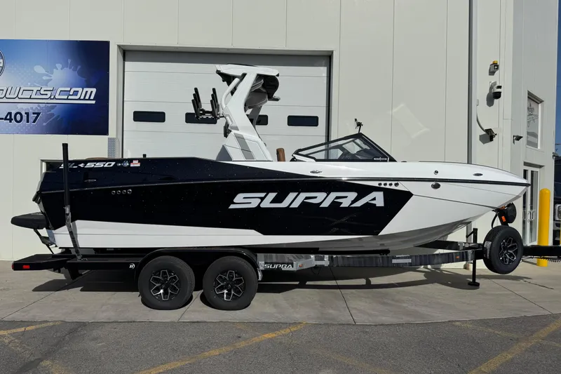 The Image of 2026 Supra SL 575 boat on trailer, parked outside a building. - 1