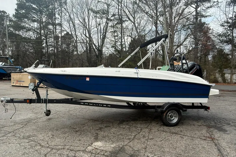 Slide: The Image of 2021 Bayliner Element E18 boat on trailer, parked outdoors with trees in background. - 2
