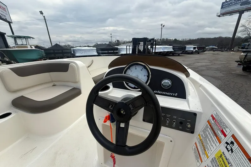 Slide: The Image of 2021 Bayliner Element E18 boat dashboard with steering wheel and gauges, parked outdoors. - 6