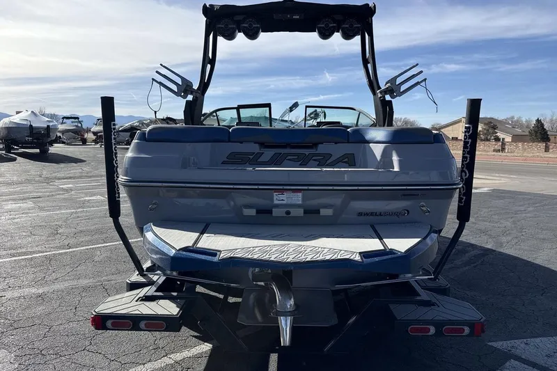Slide: The Image of 2019 Supra SR boat rear view in parking lot, showcasing wakeboard tower and swim platform. - 4