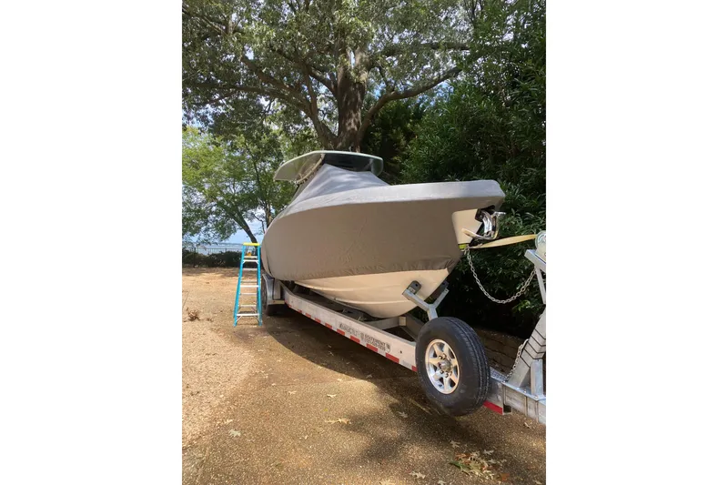 Slide: The Image of 2023 Statement 350 Open boat covered on trailer, parked outdoors under trees. - 30