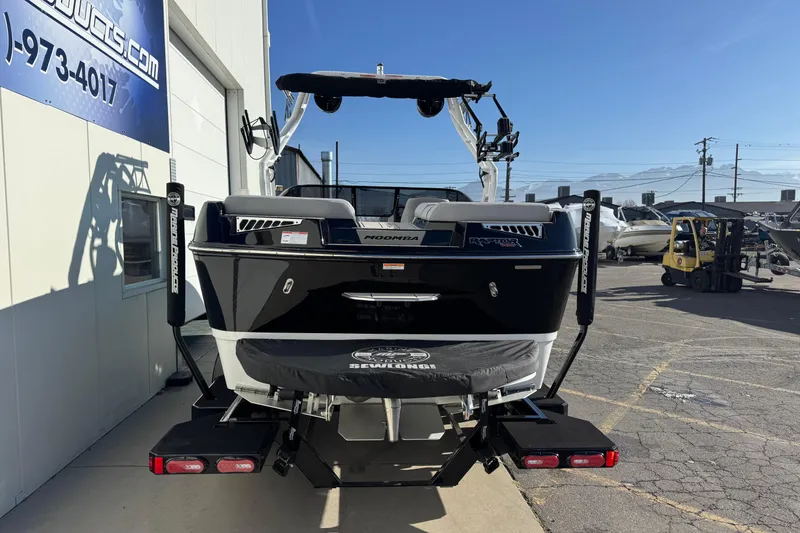 Slide: The Image of 2026 Moomba Mojo boat, black exterior, parked outside a marine dealership. - 2