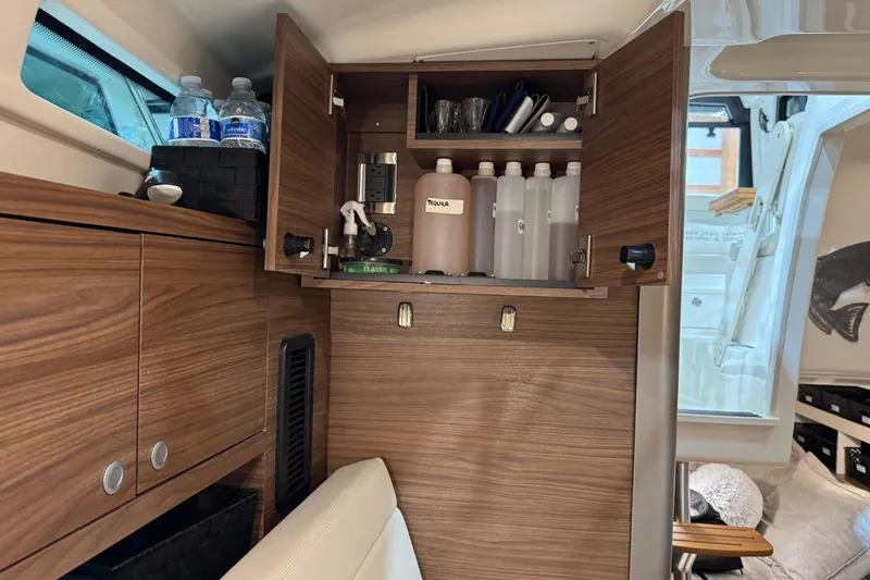 Slide: The Image of 2022 Boston Whaler 325 Conquest Pilothouse interior with open wooden cabinet and storage. - 13