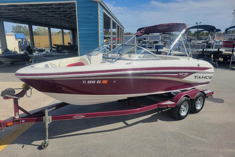 The Image of 2014 Tahoe Q7i boat on trailer at marina, featuring maroon and white design. - 1
