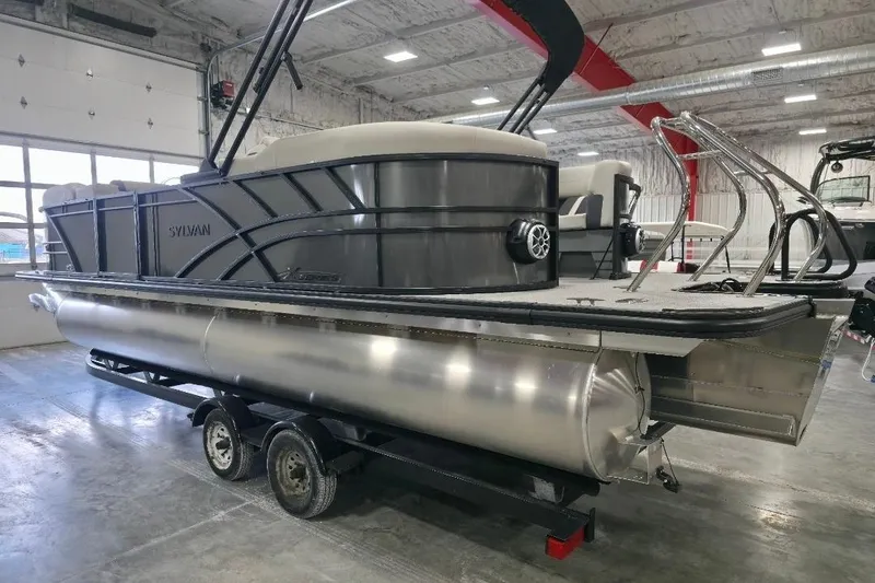 Slide: The Image of 2026 Sylvan Mirage X5 pontoon boat in showroom, on trailer, with sleek design. - 2