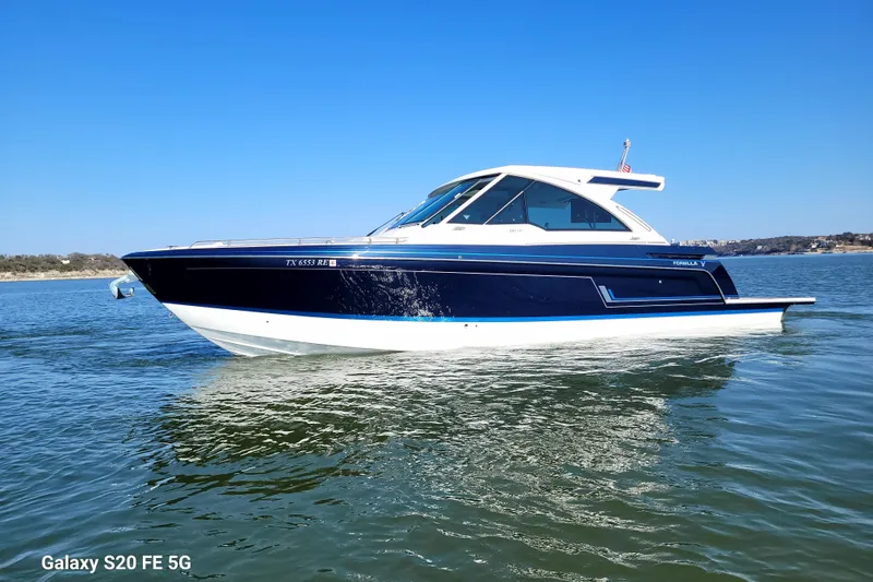 Slide: The Image of 2023 Formula 380 Super Sport Crossover I/O boat on calm water under clear blue sky. - 1
