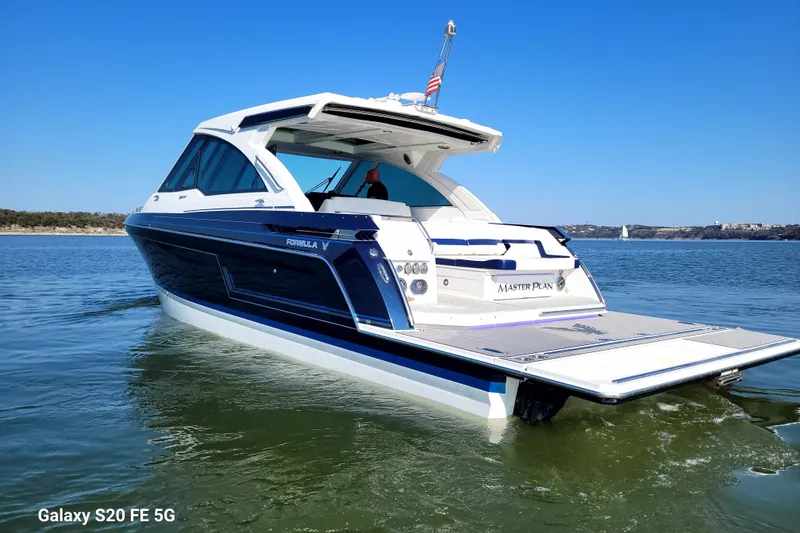 Slide: The Image of 2023 Formula 380 Super Sport Crossover I/O boat on calm water, clear blue sky. - 14