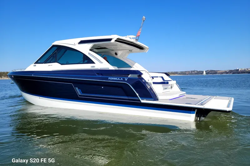 Slide: The Image of 2023 Formula 380 Super Sport Crossover I/O boat on calm water under clear blue sky. - 15