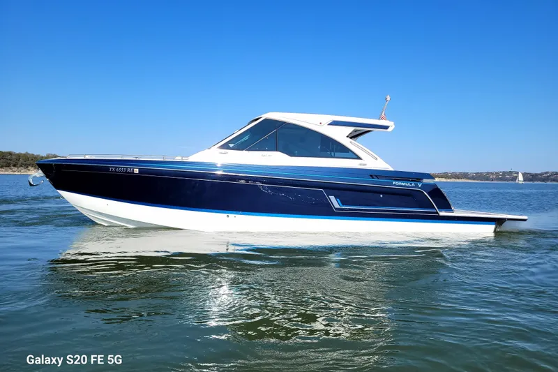 Slide: The Image of 2023 Formula 380 Super Sport Crossover I/O boat on calm water under clear blue sky. - 16