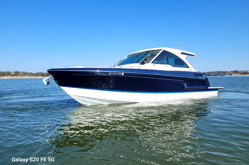 Slide: The Image of 2023 Formula 380 Super Sport Crossover I/O boat on calm water under clear blue sky. - 2