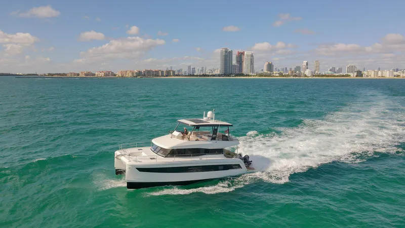 Slide: The Image of 2022 Fountaine Pajot MY6 yacht cruising on turquoise waters near a city skyline. - 2
