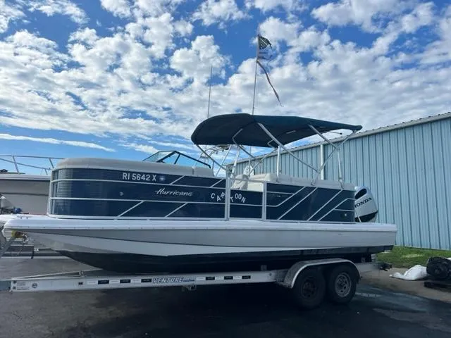 Slide: The Image of 2020 Hurricane FunDeck 236SB OB boat on trailer, blue and white, docked near a blue building. - 0