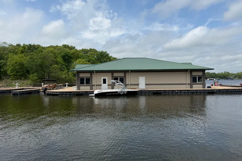 Slide: The Image of 2008 Nautique Super Air Nautique 220 docked by a lakeside building under a cloudy sky. - 16