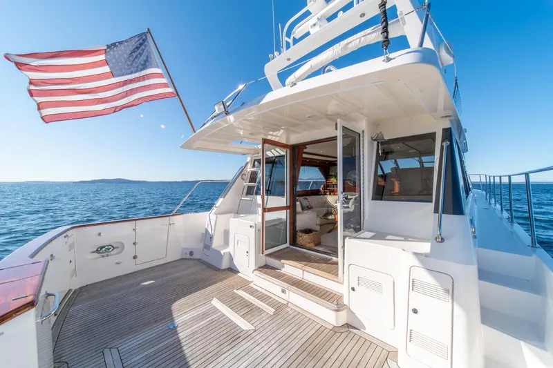 Slide: The Image of 1998 West Bay 58 Sonship Pilothouse MY yacht with American flag, open deck, and ocean view. - 56