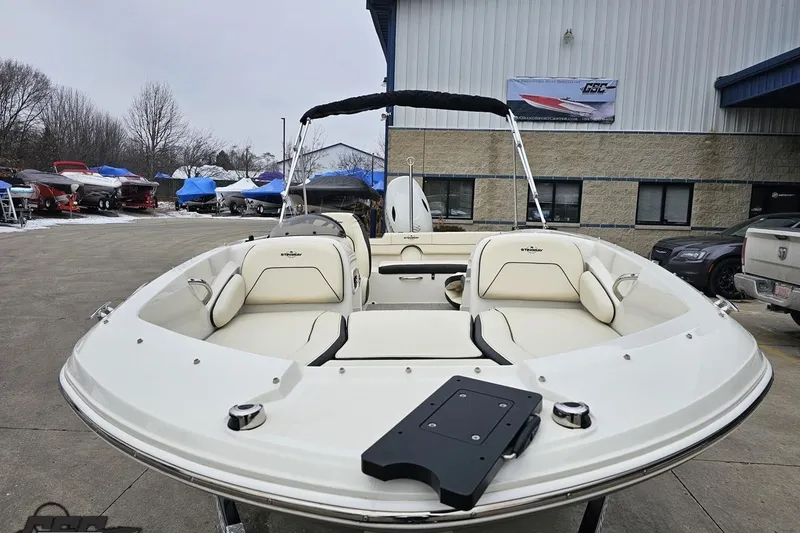 Slide: The Image of 2022 Stingray 182 SC boat with white seating, parked outdoors near a building. - 14
