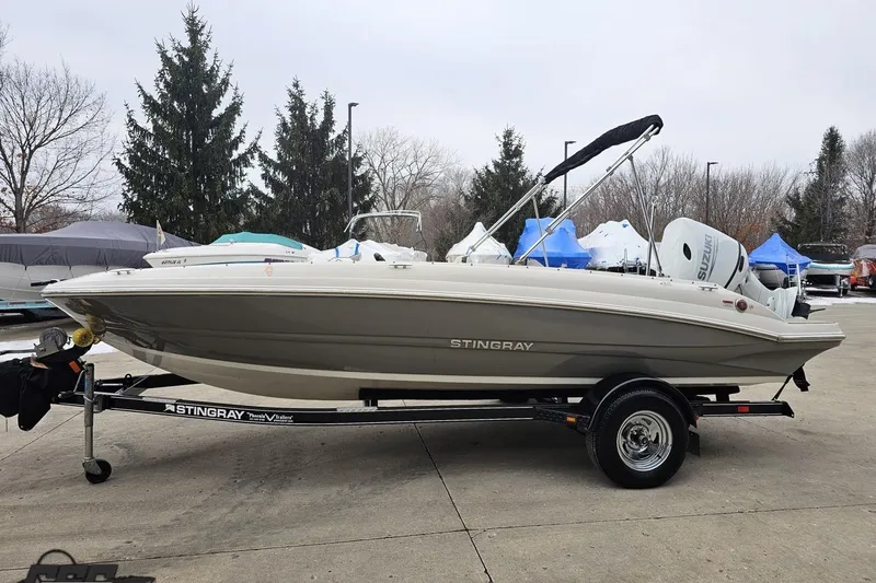 Slide: The Image of 2022 Stingray 182 SC boat on trailer, parked outdoors with trees in background. - 18