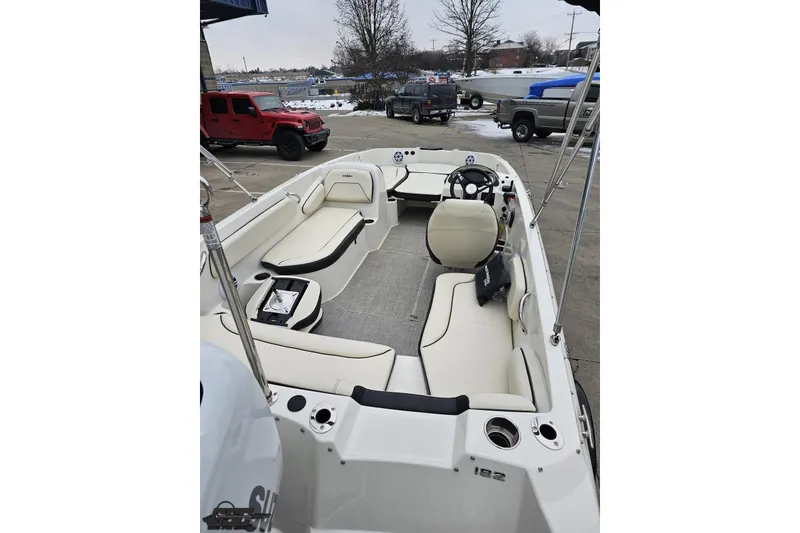 Slide: The Image of 2022 Stingray 182 SC boat interior with seating and steering wheel, parked outdoors. - 33