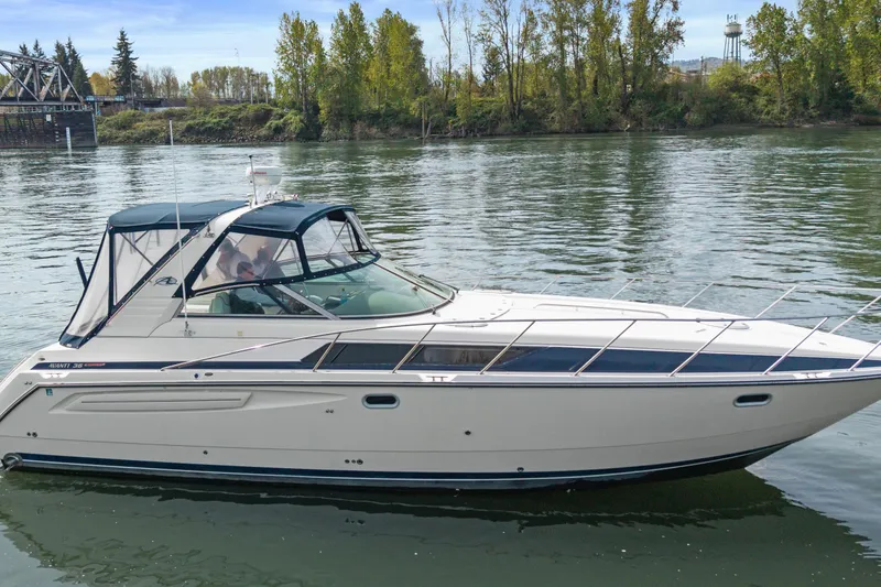 The Image of 1998 Bayliner 3685 Avanti Sunbridge cruising on a calm river with lush green trees. - 0