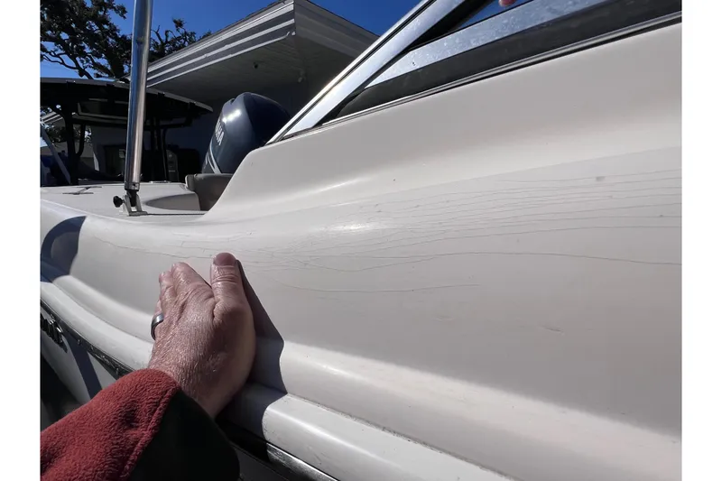 Slide: The Image of Hand inspecting 2008 Scout 205 Dorado boat exterior with visible surface lines. - 10