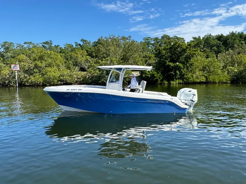 The Image of 2022 Aquasport 2500 Center Console boat on calm water with lush greenery in the background. - 1