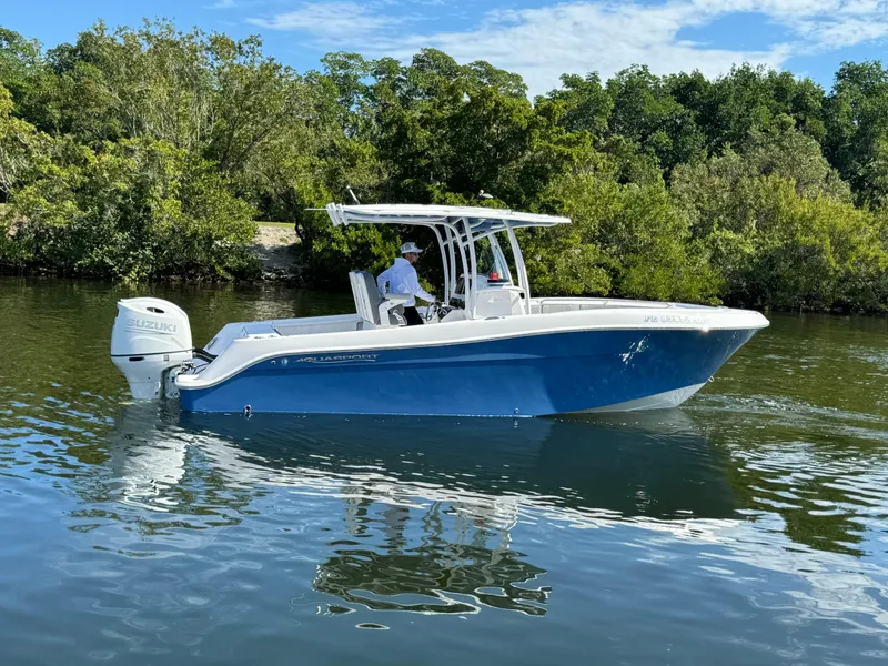 Slide: The Image of 2022 Aquasport 2500 Center Console boat on calm water near lush greenery. - 5
