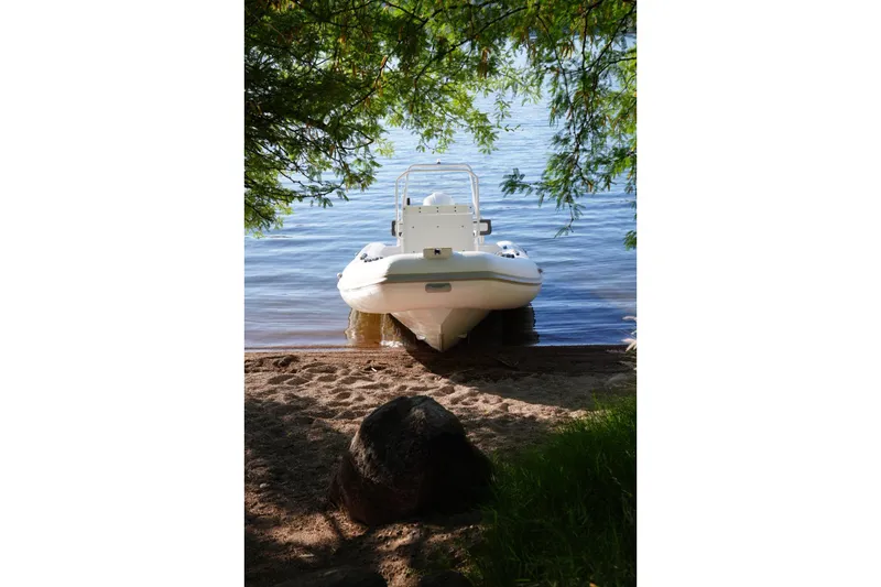 Slide: The Image of Tide Craft Sanibel 17 boat docked on a sandy lakeshore, surrounded by greenery, 2026 model. - 7