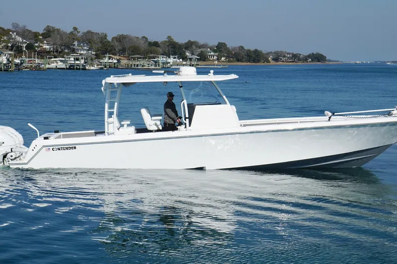 Slide: The Image of 2024 Contender 39 ST boat cruising on a calm blue lake near a residential shoreline. - 10