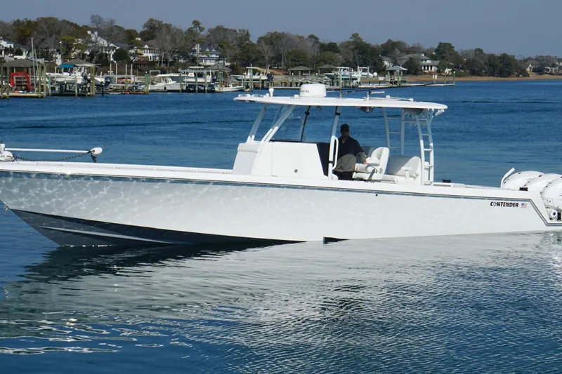 Slide: The Image of 2024 Contender 39 ST boat cruising on a calm blue lake near a marina. - 4