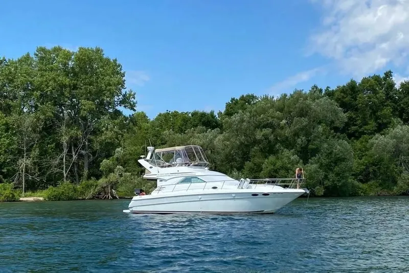 Slide: The Image of 2000 Sea Ray 400 Sedan Bridge yacht on a serene lake with lush green trees. - 3