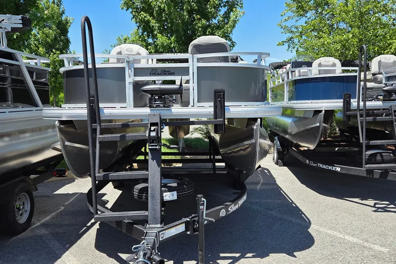 Slide: The Image of 2026 Sun Tracker Bass Buggy 16 XL Select pontoon boat on trailer, parked outdoors. - 2