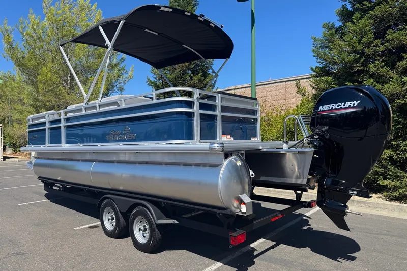 Slide: The Image of 2026 Sun Tracker SportFish 22 DLX pontoon boat with Mercury outboard motor in a parking lot. - 2