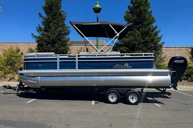 The Image of 2026 Sun Tracker SportFish 22 DLX pontoon boat on trailer, parked outdoors. - 0