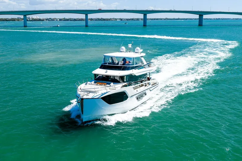 Slide: The Image of Luxury 2022 Absolute 64 Navetta yacht cruising under a bridge on clear blue waters. - 19