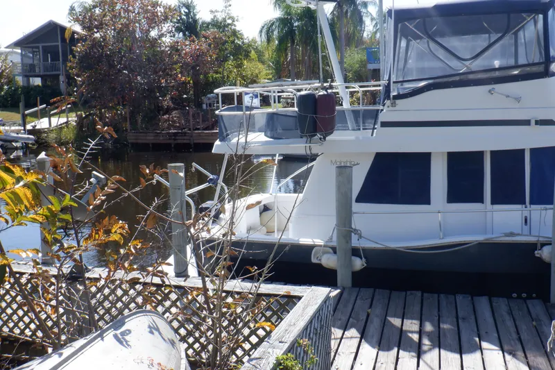 Slide: The Image of 1999 Mainship 350 Trawler docked by a wooden pier, surrounded by lush greenery. - 4