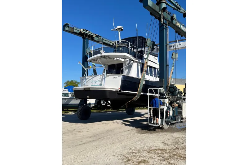 Slide: The Image of 1999 Mainship 350 Trawler being lifted by a boat hoist at a marina. - 58