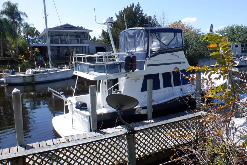 Slide: The Image of 1999 Mainship 350 Trawler docked by a waterfront home, surrounded by lush greenery. - 6