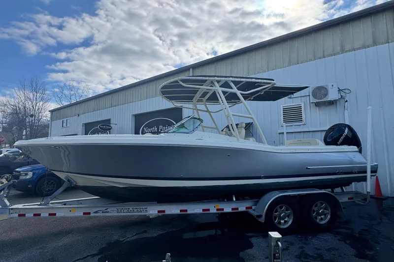 Slide: The Image of 2017 Chris-Craft Calypso 26 boat on trailer, parked outside a building under a cloudy sky. - 2