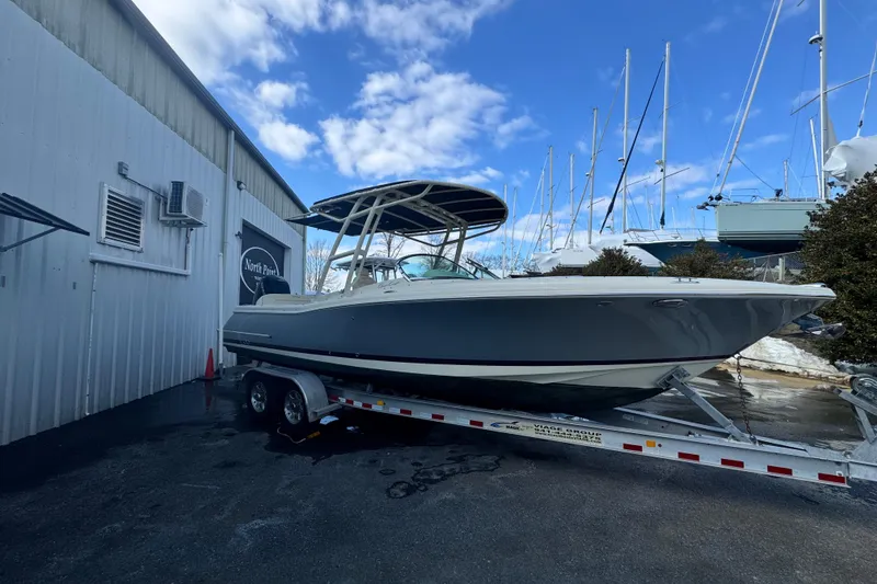 Slide: The Image of 2017 Chris-Craft Calypso 26 boat on trailer, parked near a marina under blue sky. - 4