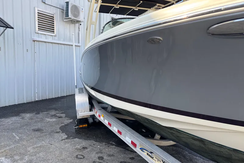 Slide: The Image of 2017 Chris-Craft Calypso 26 boat on trailer, parked near a metal building. - 44