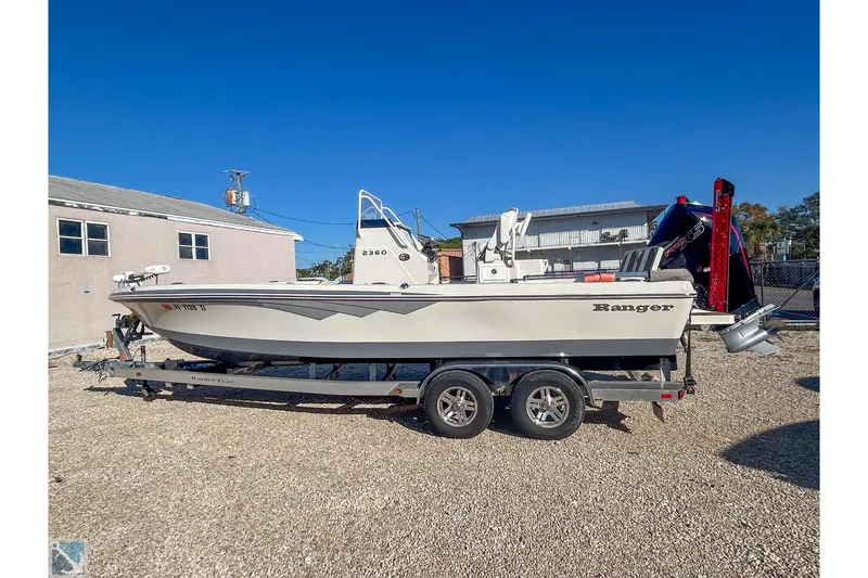 The Image of 2022 Ranger 2360 Bay boat on trailer, parked outdoors under clear blue sky. - 1