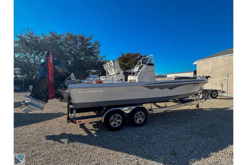 Slide: The Image of 2022 Ranger 2360 Bay boat on trailer, parked outdoors under clear blue sky. - 3