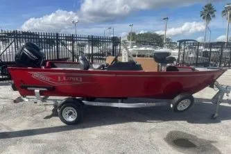 The Image of 2026 Lund 1650 Angler SS boat in red, parked on a trailer, with a scenic marina backdrop. - 1