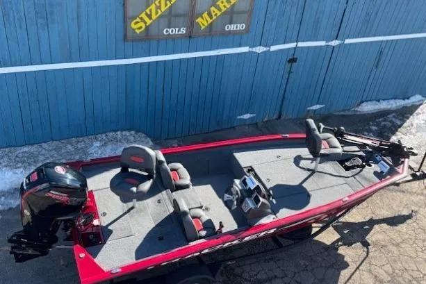 Slide: The Image of 2025 Tracker Pro Team 190 boat with red trim, parked near a blue wooden building. - 5